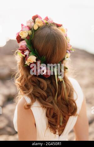 Bride with a wreath of roses on her head, back view. A flower wreath on the head of a girl for brown hair. Stock Photo