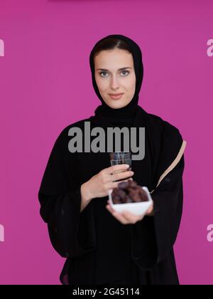 Modern muslim woman in abaya holding a date fruit and glass of water in front of her Stock Photo