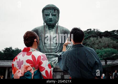 Koutokuin Temple with couple in foreground taking a photo of Buddha statue, Toyko, Japan Stock Photo