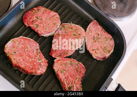 Four raw steaks are fried on a grilled pan. Stock Photo