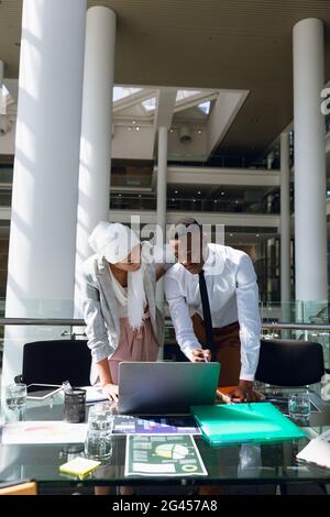 Male and female executives discussing over laptop at desk Stock Photo