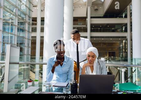 Male and females executives discussing over laptop at desk Stock Photo