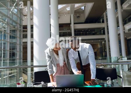 Male and female executives discussing over laptop at desk Stock Photo