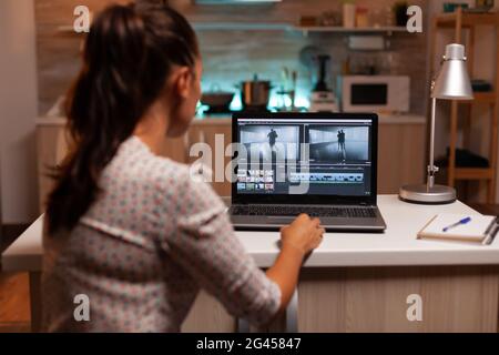 Back view of creative filmmaker working on a movie on laptop during midnight. Content creator in home working on montage of film using modern software for editing late at night. Stock Photo