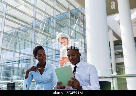 Male and females executives discussing over digital tablet at desk Stock Photo