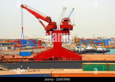 A large red crane used in importing and exporting, three tug boats and a container area are in this photo of the Port of Lomé, Togo, West Africa. Stock Photo