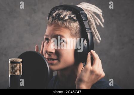 Happy positive guy with dreadlocks is recording a song in the studio. A young attractive singer in black studio headphones stands in front of a microp Stock Photo
