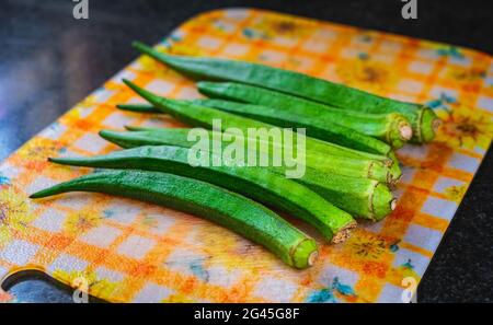 Selective focus of a few pods of okra placed on a plastic cutting board. Black granite background. Stock Photo