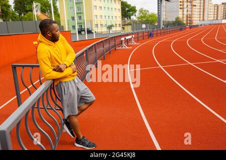 Handsome African American runner athlete in yellow sportswear having a break, doing running training, preparing for important competition at stadium Stock Photo