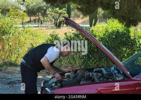 mature man fixing a breakdown in his car engine with tools on the side of the road Stock Photo