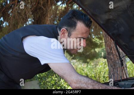 mature man fixing a breakdown in his car engine with tools on the side of the road Stock Photo