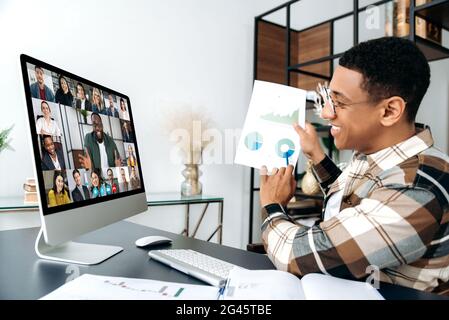 Distant online meeting, business negotiations. Hispanic young successful man, ceo or entrepreneur, communicates with his multiracial business team by video call, shows a graph, profit report Stock Photo