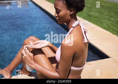 Woman using sunscreen while sitting by the pool Stock Photo