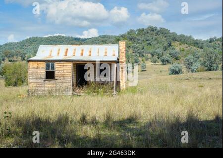An abandoned, pioneer settler wooden farmhouse with corrugated iron roof on a hillside in the New England Tablelands of New South Wales in Australia. Stock Photo