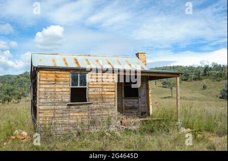 An abandoned, pioneer settler wooden farmhouse with corrugated iron roof on a hillside in the New England Tablelands of New South Wales in Australia. Stock Photo