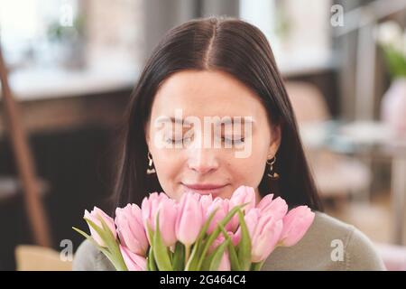 Happy young brunette female smelling bunch of pink tulips Stock Photo