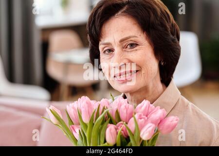 Happy mature woman with bouquet of pink tulips looking at you Stock Photo