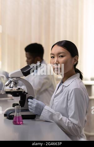 Young serious woman in lab coat and gloves working in scientific laboratory Stock Photo