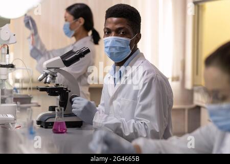 Young African male chemist in protective workear using microscope Stock Photo