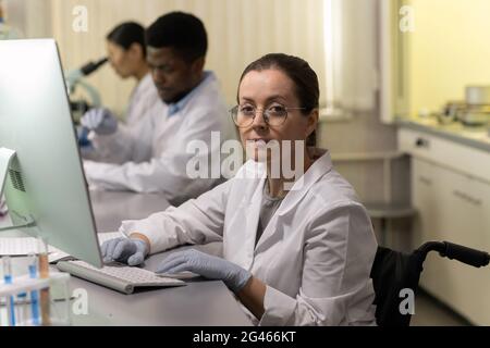 Confident female chemist using computer by workplace against two colleagues Stock Photo