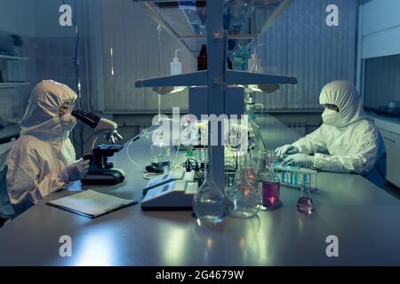 Two contemporary lab workers in coveralls using microscope and laptop Stock Photo