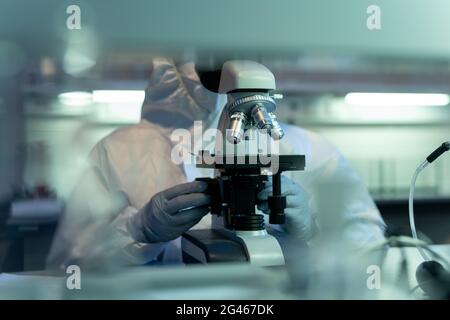 Gloved hands of scientist in coveralls using microscope Stock Photo