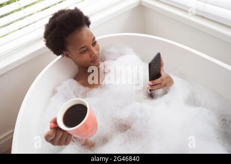 Woman with coffee cup using smartphone in a bathtub Stock Photo