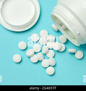 Round white pills spilled out of a plastic jar on a blue background Stock Photo