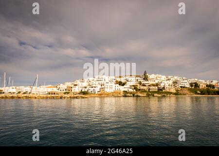 Naoussa coastal village (Paros Island) landscape view during golden hour with typical whitewashed cycladic houses and dramatic sky seen from the sea, Stock Photo