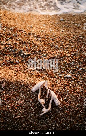 Bridal sandals with thick heels decorated with stones on a pebble beach on the sea. Stock Photo