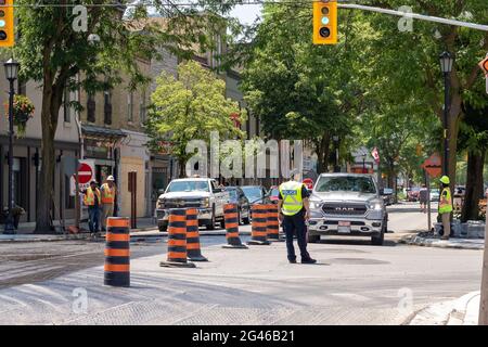 Strathroy, Ontario, Canada - June 11 2021: Police Officer directing traffic in the middle of an intersection at construction site. Traffic light green. Stock Photo