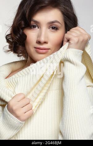 Brunette beautiful woman dressed in large white woolen sweater on gray background. Stock Photo