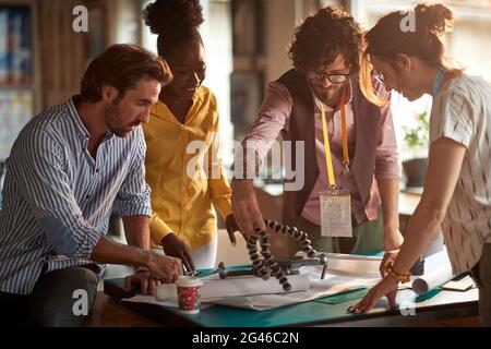 A group of young creative people in a working atmopshere in the office are observing new gadgets they will use in the project. Employees, office, work Stock Photo