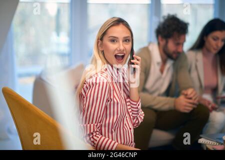 A young beautiful businesswoman surprised by a phone call at a meeting in a relaxed atmosphere with her colleagues. People, business, meeting Stock Photo
