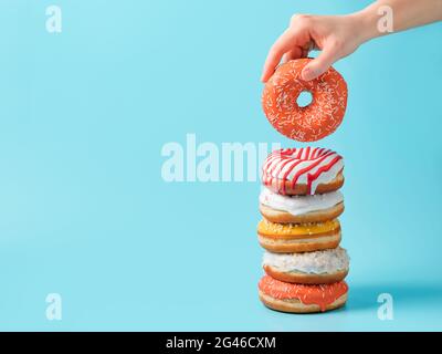 Stack of donuts, donut in hand on blue, copy space Stock Photo