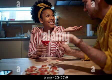 young adult multiethnic couple drinking wine after dinner at home, talking, smiling. valentine, date, at home, lockdown concept Stock Photo