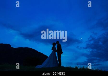 Silhouette of the newlyweds against the sky at sunset. Wedding i Stock Photo