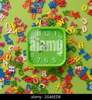 Square alarm clock and multicolored wooden letters of the english alphabet on a green background Stock Photo