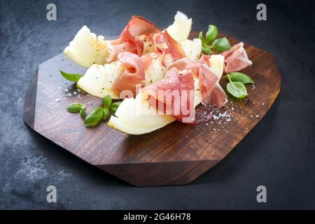 Traditional Italian antipasti with prosciutto di Parma and honeydew melon slices offered as close-up on a wooden design board Stock Photo