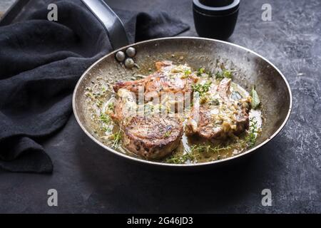 Traditional barbecue dry aged veal chops with herbs in butter jus served as close-up in a rustic iron pan on a black board Stock Photo