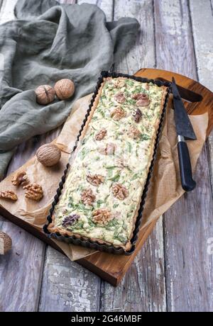 Traditional French Autumn walnut spinach tarte served as close-up in a backing form on an Modern design wooden board Stock Photo
