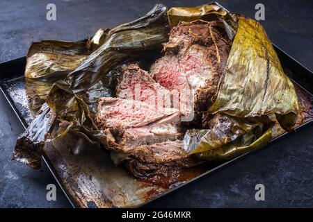 Slow cooked Omani lamb shuwa coated in rub of spices and wrapped in banana leaves sliced and served as close-up on a rustic meta Stock Photo