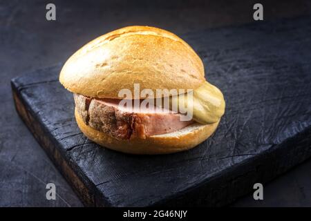 Traditional oven-fresh Bavarian leberkaese sliced in a roll with hot mustard served as close-up on an old rustic wooden board wi Stock Photo