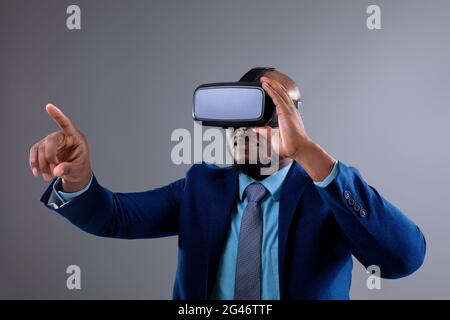 African american businessman wearing vr headset touching invisible screen against grey background Stock Photo