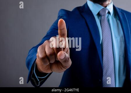 Mid section of african american businessman touching invisible screen against grey background Stock Photo