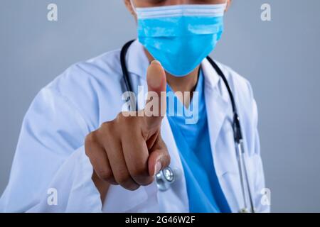Mid section of doctor wearing face mask touching invisible screen against grey background Stock Photo