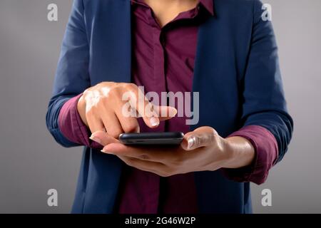 Mid section of businesswoman using a smartphone against grey background Stock Photo