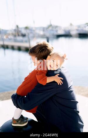 An adorable 2-year old girl is hugging her father at a boat marina Stock Photo