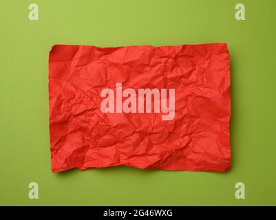 Crumpled rectangular sheet of red paper on a green background, top view Stock Photo