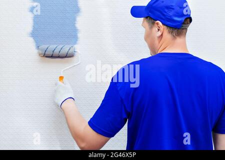 Service Repair and restoration of premises. Portrait of a house painter and a paint roller painting the wall in blue. Stock Photo